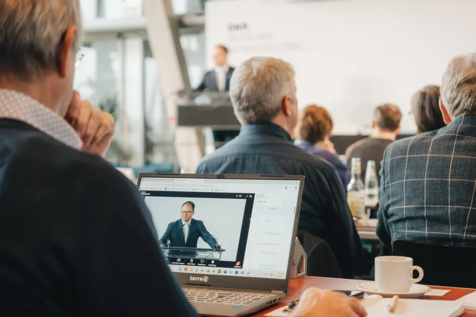 Blick auf einen Laptop mit Livestream der Rede von Umweltminister Carsten Schneider, der zusätzlich im Hintergrund am Podium steht